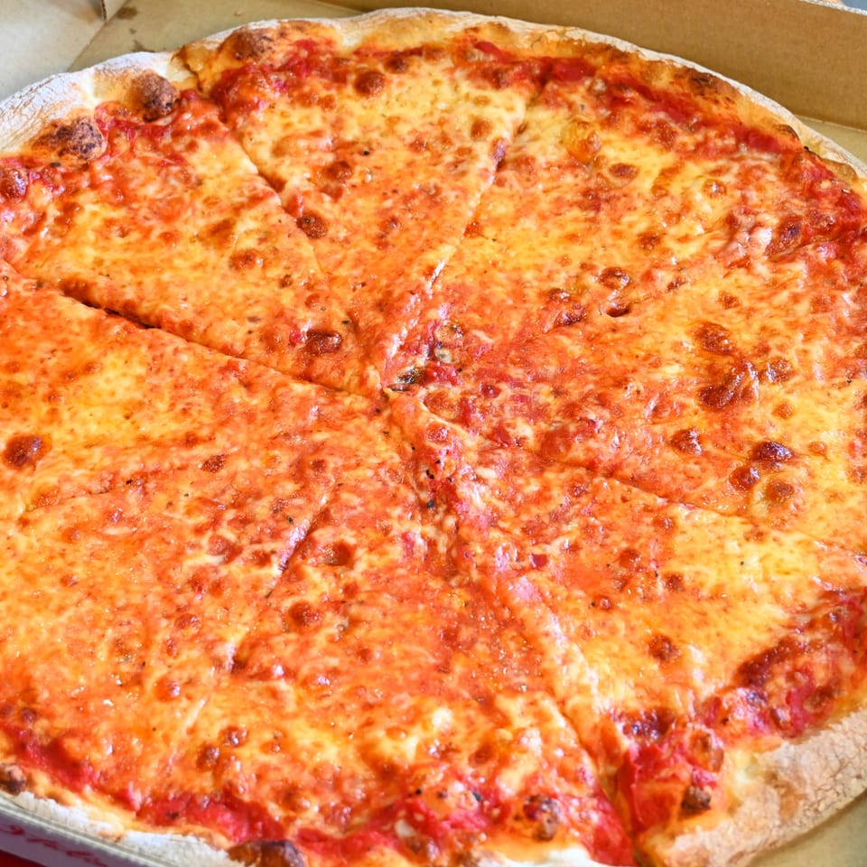 Large rectangular cheese pizza with tomato sauce and browned mozzarella, cut into square slices in a cardboard box.