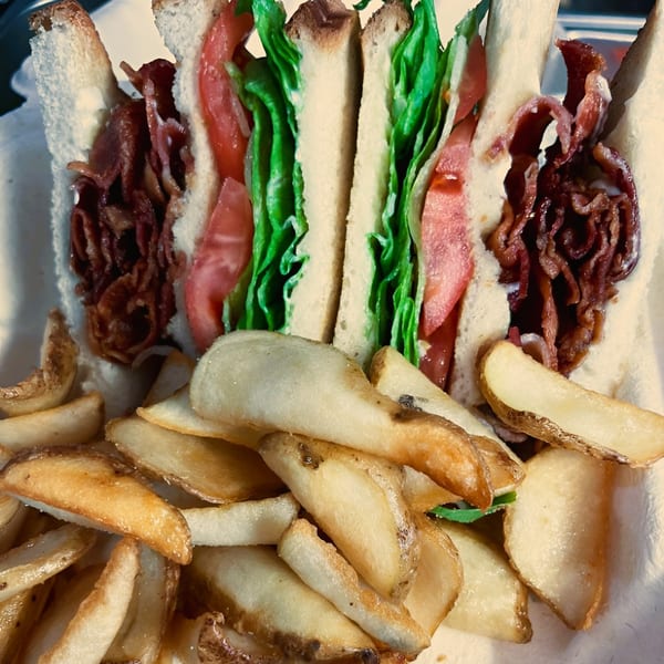 A BLT sandwich with crispy bacon, lettuce, and tomato, served with a side of potato wedges.