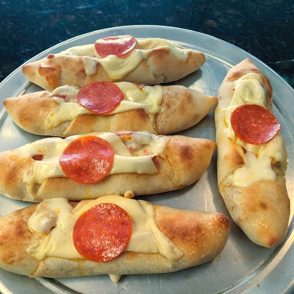 Five Jace's Place pepperoni pizza rolls with melted cheese on a metal tray.