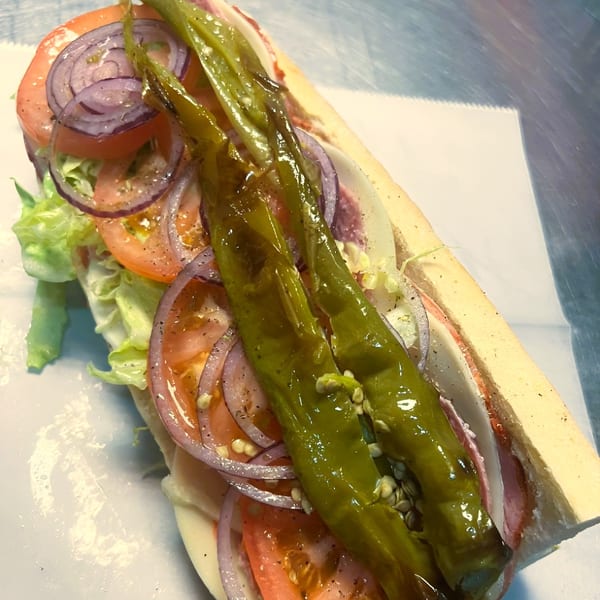 A Jace's Place sub sandwich with green peppers, red onions, tomatoes, lettuce, and deli meat.