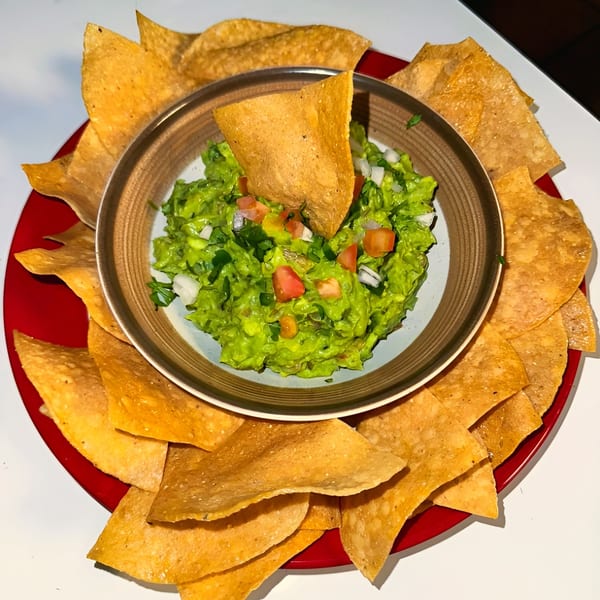 Guacamole with diced tomatoes and onions, surrounded by tortilla chips on a red plate.