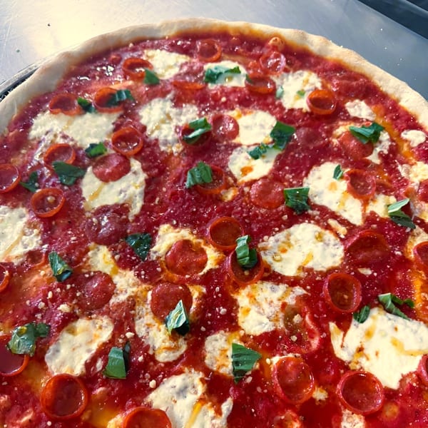Close-up of a Jace's Place pepperoni pizza with fresh basil and melted mozzarella cheese.