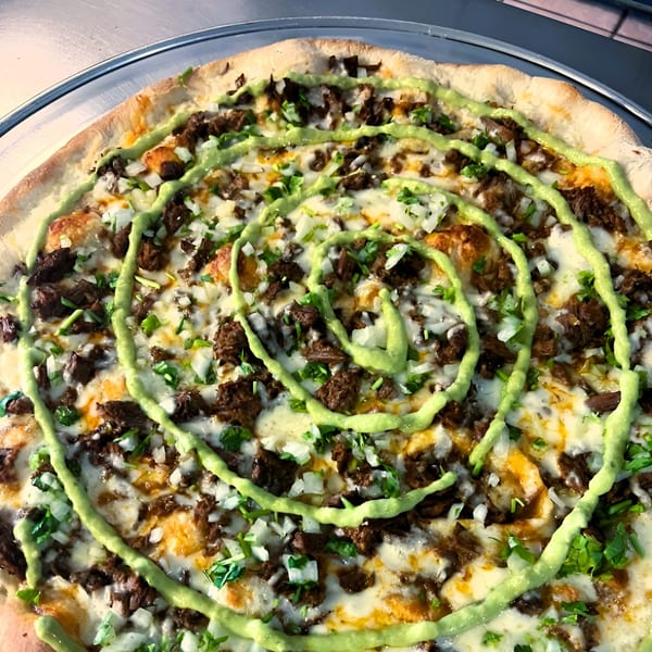 Jace's Place pizza with meat, cheese, diced onions, cilantro, and a spiral of green sauce.