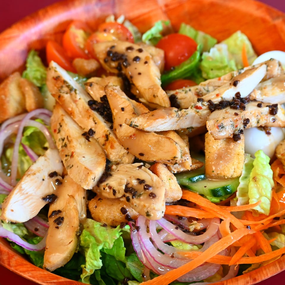 Grilled chicken strips with black pepper served over lettuce, tomatoes, cucumbers, carrots, and red onions.