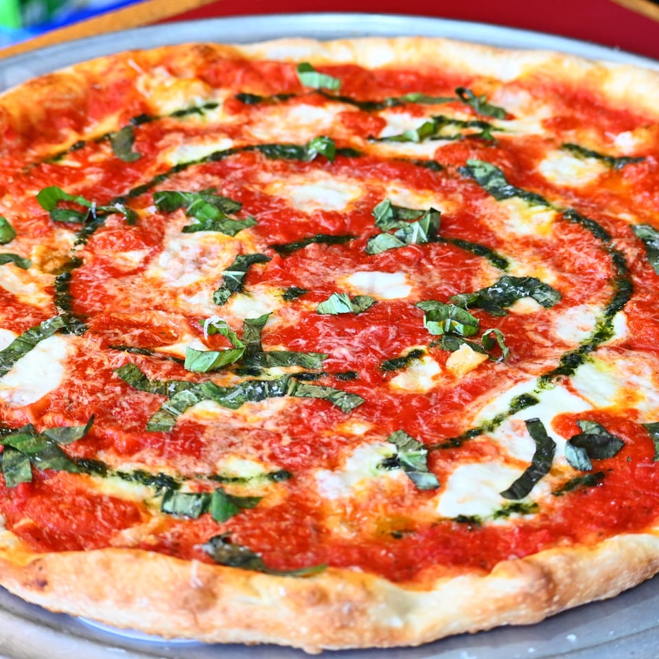 Close-up of a thin-crust pizza topped with tomato sauce, melted cheese, and fresh basil leaves.