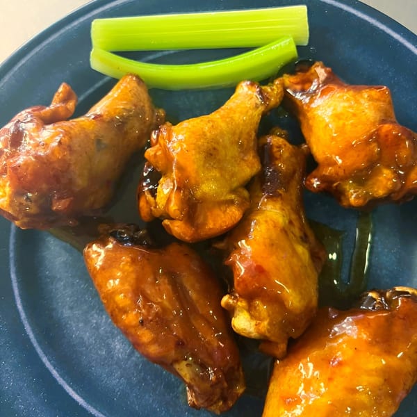 Six glazed chicken wings with two celery sticks on a blue plate at Jace's Place.