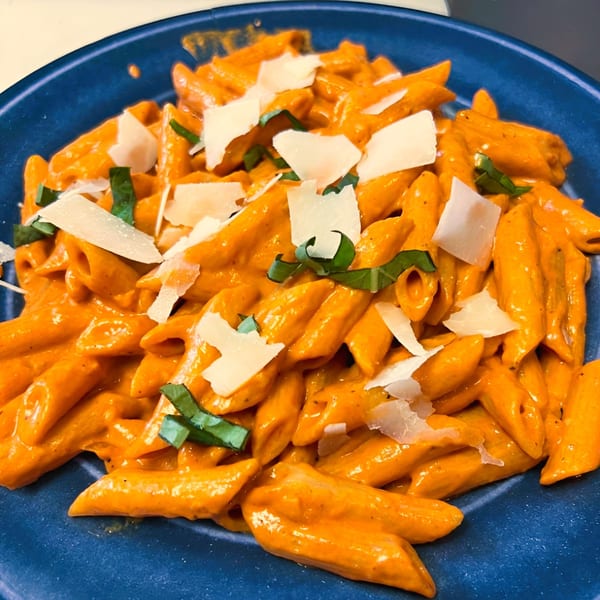 Penne pasta in a creamy orange sauce, topped with fresh basil and shaved Parmesan cheese on a blue plate.