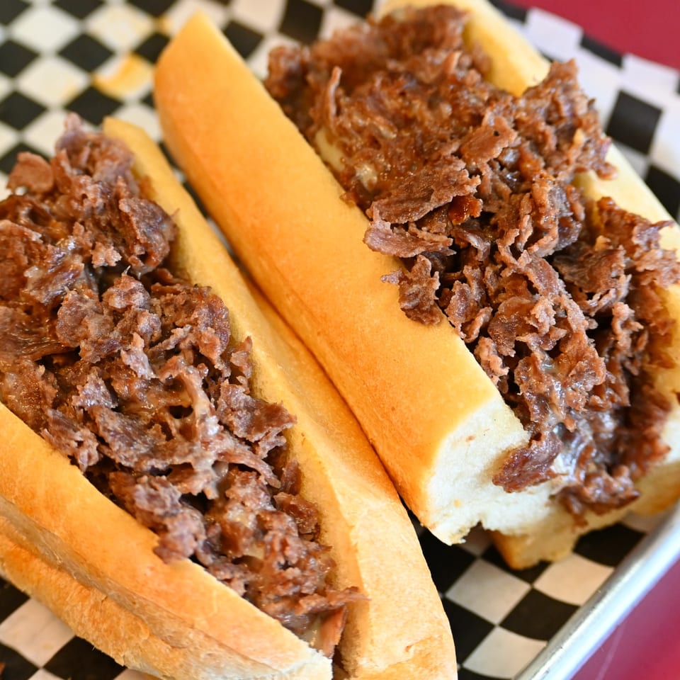 Two toasted hoagie rolls overflowing with shaved roast meat on a black-and-white checkered serving tray.