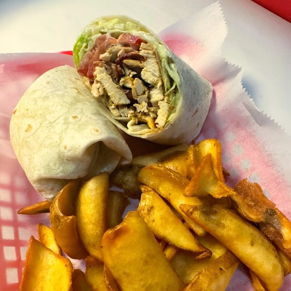 Chicken wrap with lettuce and tomatoes, served with a side of golden potato wedges.