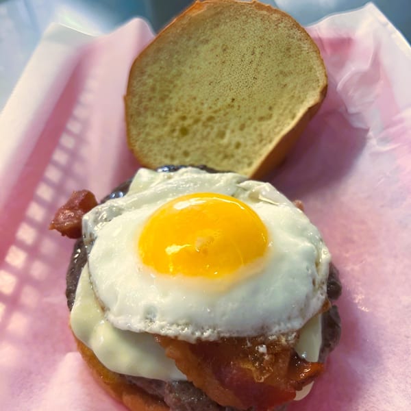A Jace's Place burger with a fried egg, bacon, and cheese, served in a pink basket.